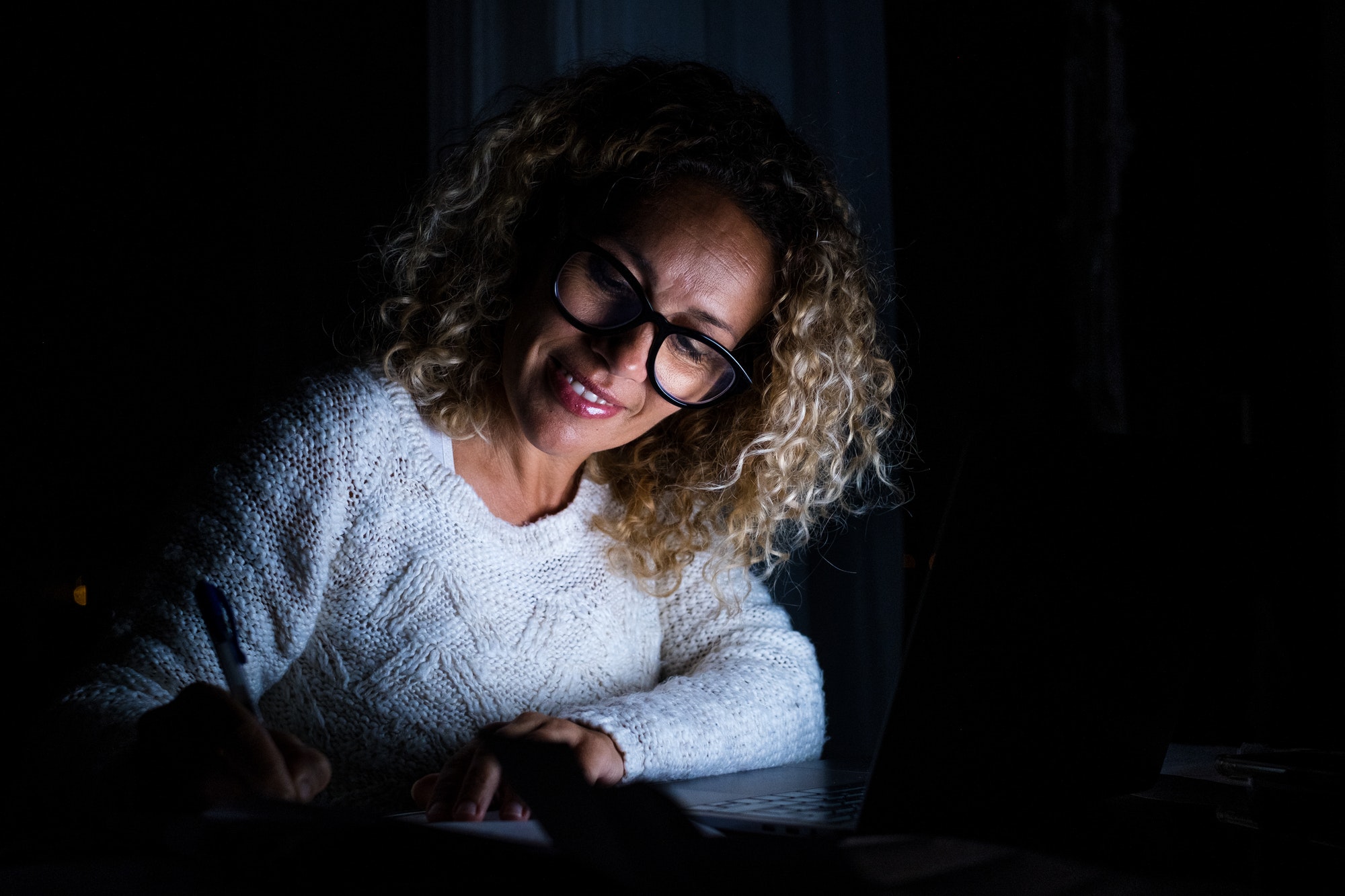 One young woman using laptop and working on a computer at night at home.